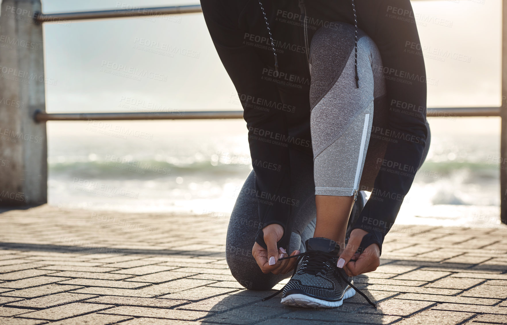 Buy stock photo Shot of a fit young woman tying her shoelaces before going for a run on the promenade