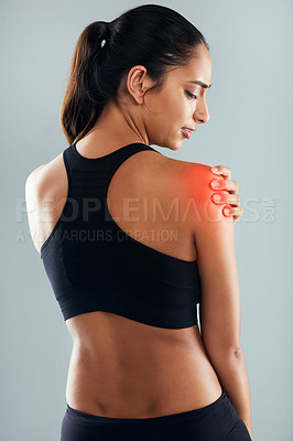Buy stock photo Rearview shot of a sporty young woman holding her shoulder in pain against a grey background