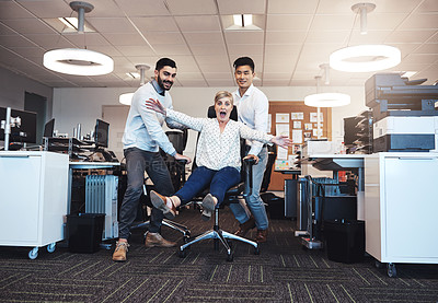 Buy stock photo Cropped shot of three businesspeople having fun by taking their colleague for a ride in her chair in the office