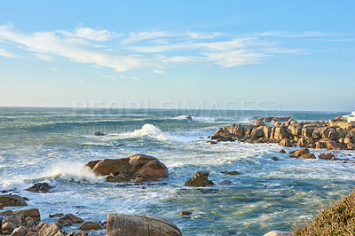 Buy stock photo Copyspace at sea with a cloudy blue sky background and rocky coast in Western Cape South Africa. Ocean waves crashing onto boulders at a beach. Peaceful scenic landscape for a relaxing summer holiday
