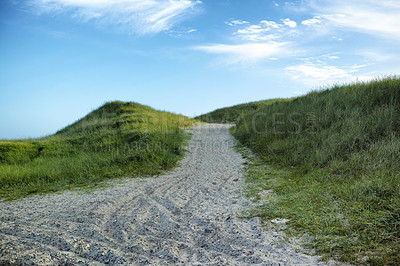 Buy stock photo Closeup of a sand path with lush green grass growing on a beach with cloudy copy space. Beautiful blue sky on a warm and sunny summer day over a dry and sandy dune situated on a coastline bay area