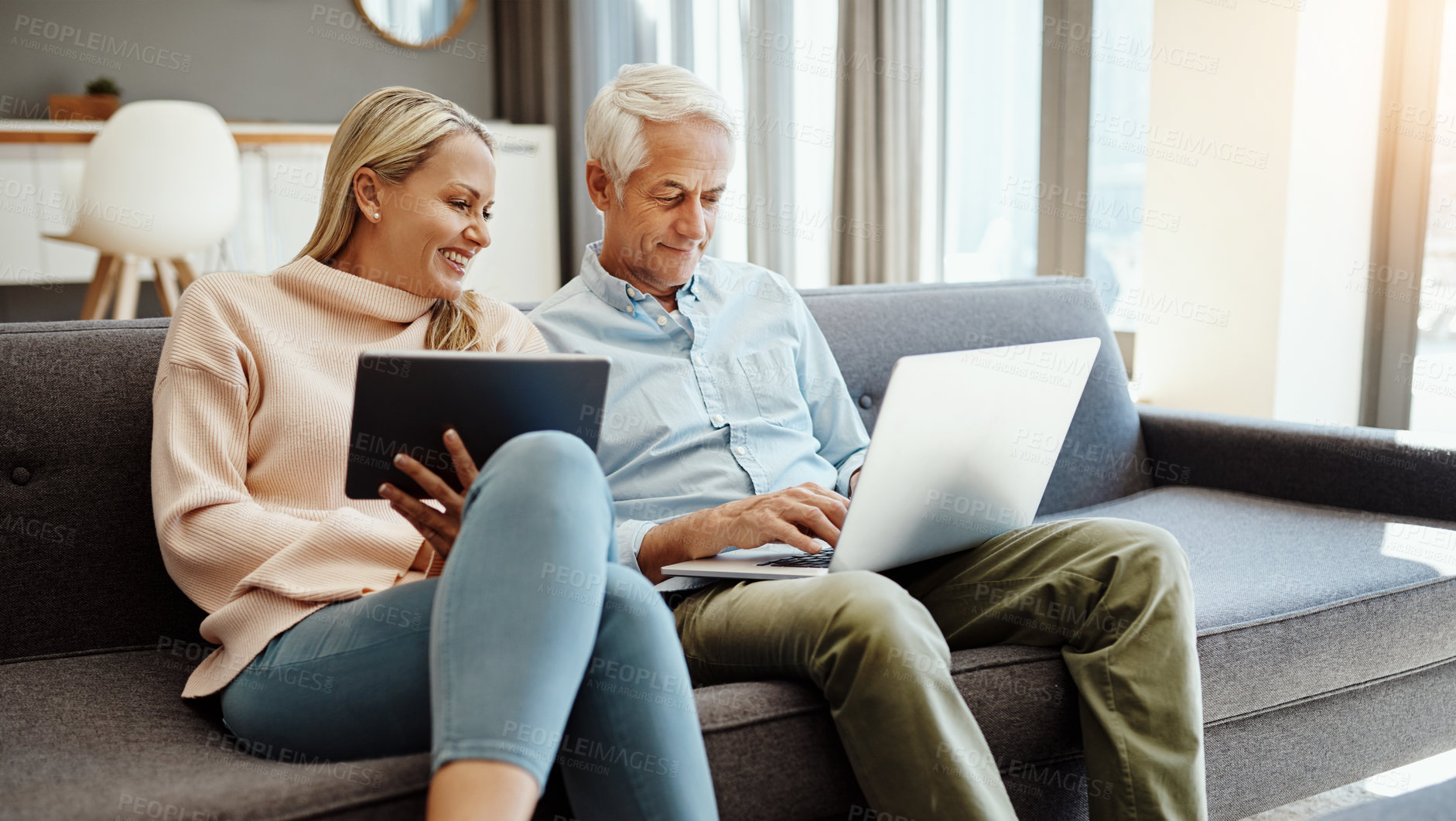 Buy stock photo Shot of a mature couple using a digital tablet and laptop on the sofa at home