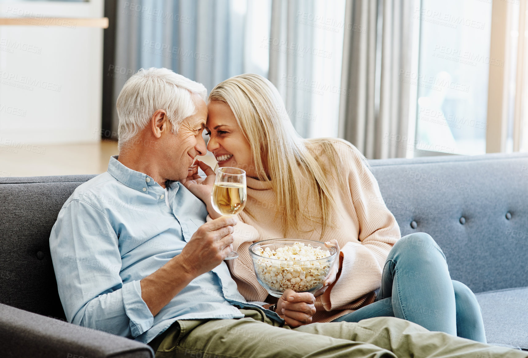 Buy stock photo Shot of a happy mature couple relaxing together with wine and popcorn on the sofa at home
