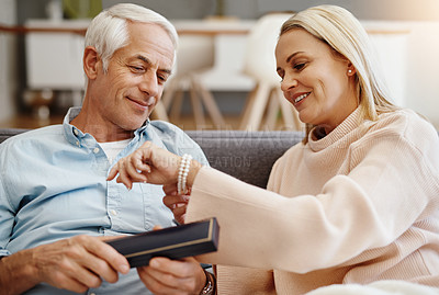 Buy stock photo Shot of mature man giving his wife a gift on the sofa at home