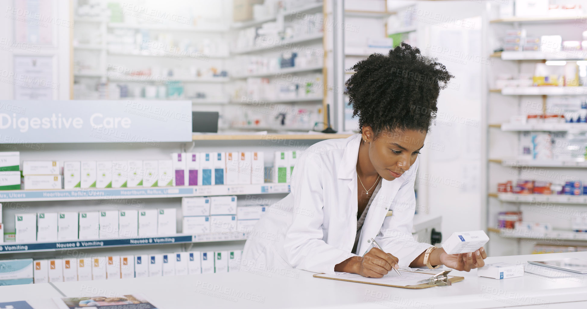 Buy stock photo Shot of an attractive young pharmacist taking notes from a box of medication