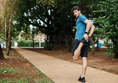 Buy stock photo Shot of a sporty young man stretching his legs while exercising outdoors