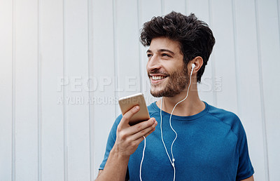 Buy stock photo Shot of a sporty young man standing against a white wall after exercising and talking on his cellphone outside during the day