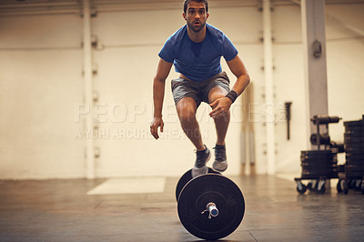 Buy stock photo Full length shot of a handsome young man balancing on a barbell while working out in the gym