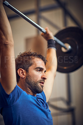 Buy stock photo Low angle shot of a handsome young man lifting weights while working out in the gym