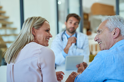Buy stock photo Shot of a cheerful senior man and his daughter having a discussion at the doctor's office