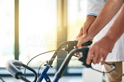 Buy stock photo Cropped shot of an unrecognizable doctor helping a senior man use a walker in his office