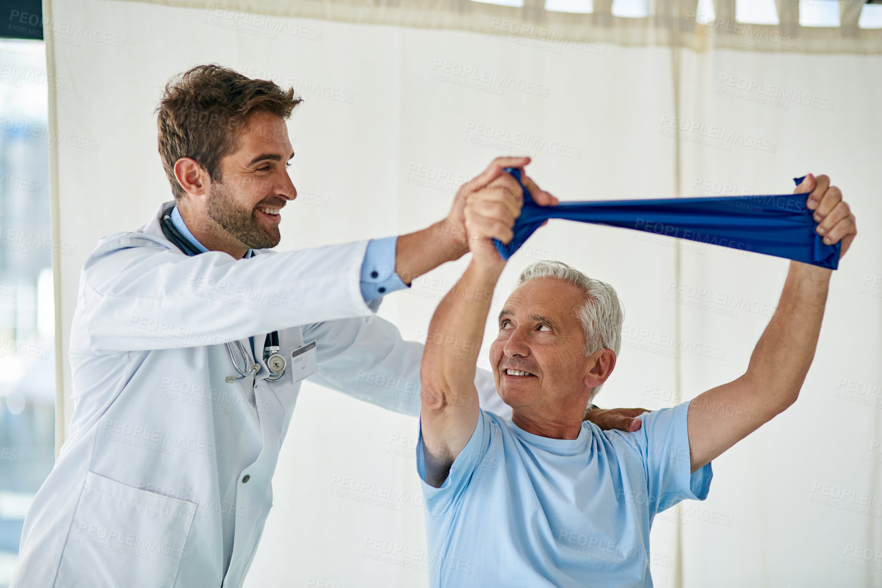 Buy stock photo Cropped shot of a friendly young doctor helping a senior man stretch with a stretching band in his office