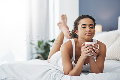 Buy stock photo Shot of an attractive young woman enjoying a cup of coffee while relaxing on her bed at home