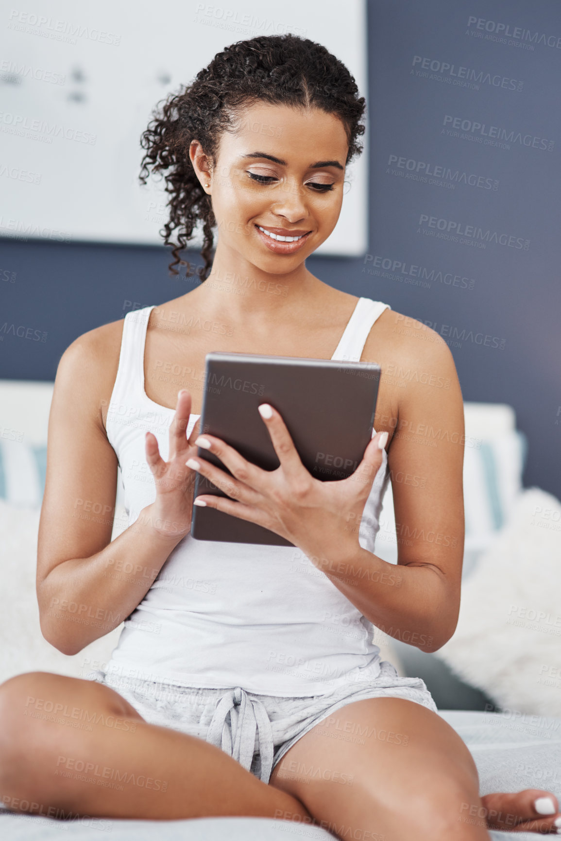 Buy stock photo Shot of an attractive young woman using her digital tablet while sitting on her bed at home