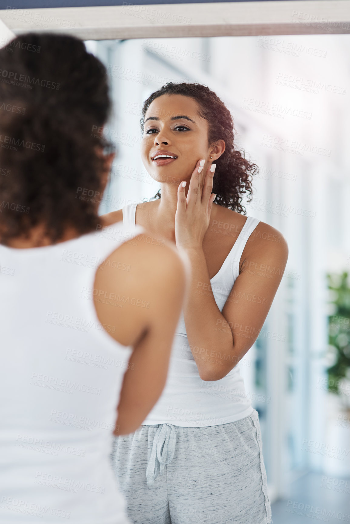 Buy stock photo Shot of an attractive young woman inspecting her face in front of the mirror in her bedroom