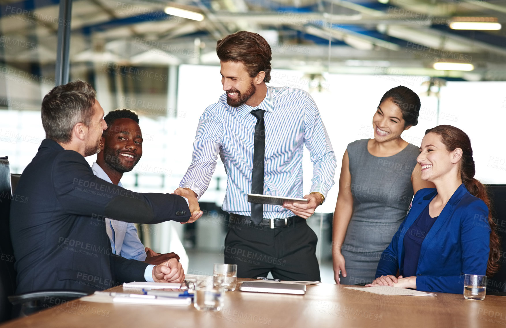 Buy stock photo Shot of two businesspeople shaking hands while in a meeting with colleagues