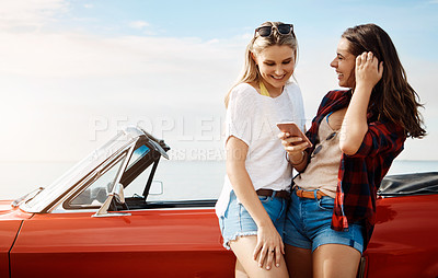 Buy stock photo Shot of two friends using a smartphone on a summer’s road trip