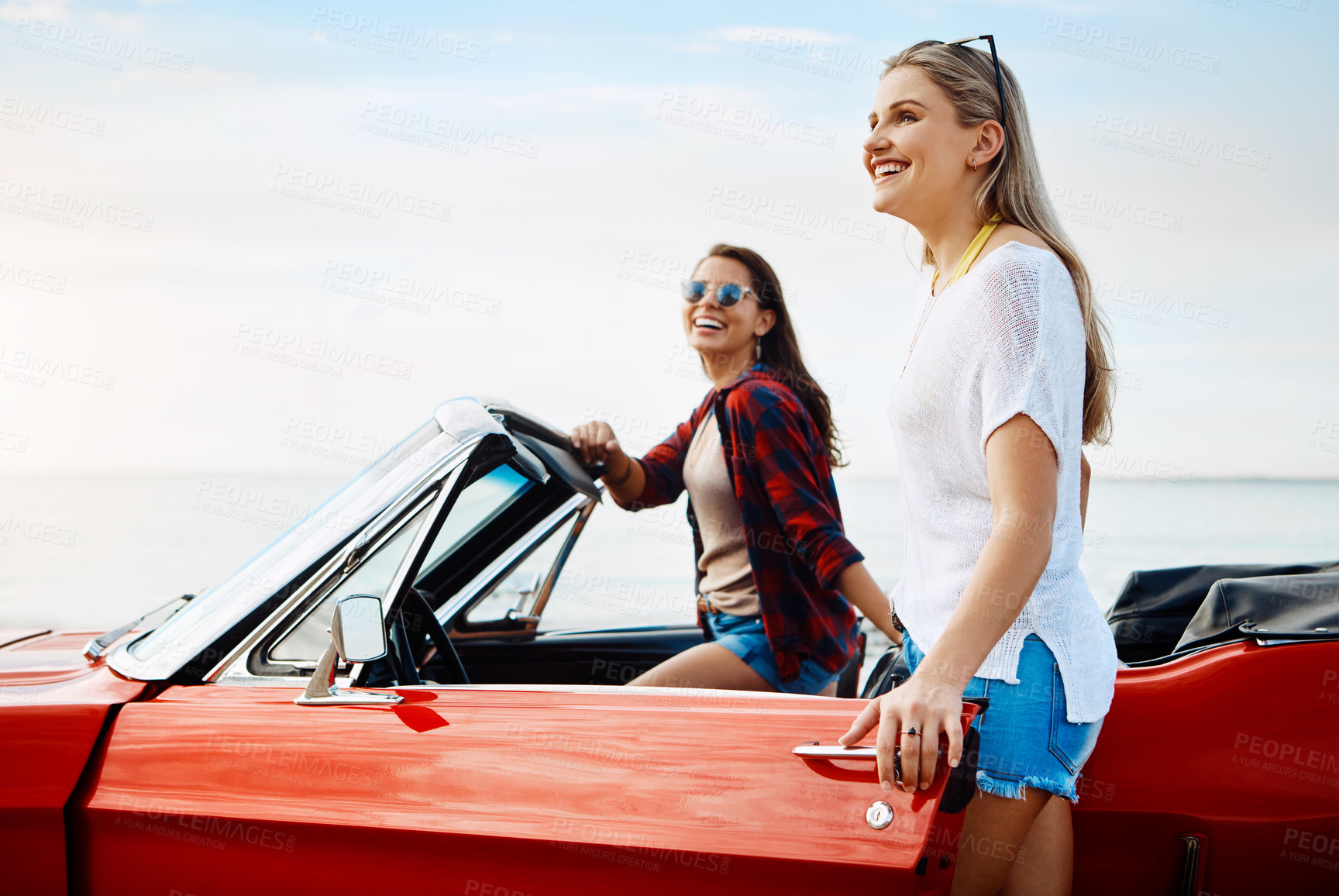 Buy stock photo Shot of a two happy young women enjoying a summer’s road trip together