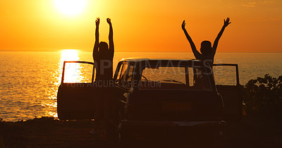 Buy stock photo Rearview shot of two unrecognizable girl friends cheering with their arms raised while on a road trip at the beach