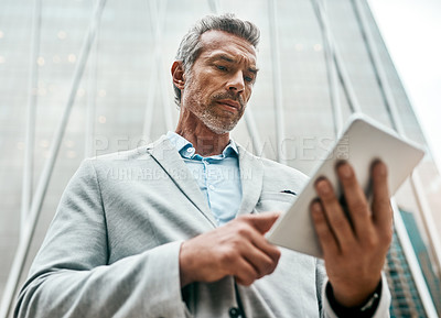 Buy stock photo Shot of a mature businessman using a digital tablet in the city