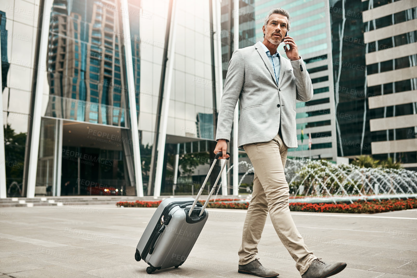 Buy stock photo Shot of a mature businessman talking on a cellphone while walking with a suitcase in the city