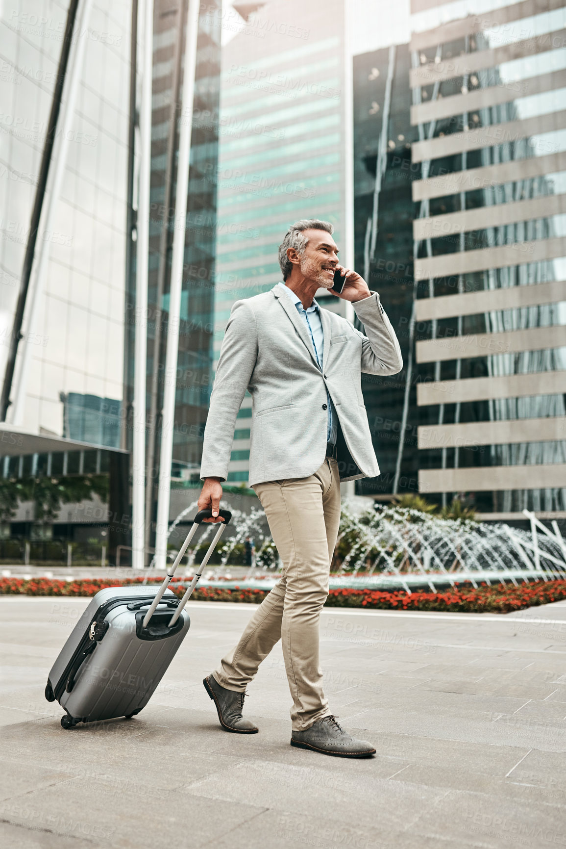 Buy stock photo Shot of a mature businessman talking on a cellphone while walking with a suitcase in the city