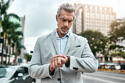 Buy stock photo Shot of a mature businessman checking the time on his wrist watch out in the city