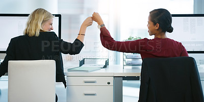 Buy stock photo Rearview shot of two young businesswomen pounding their fists in succession while being seated at their desk in the office