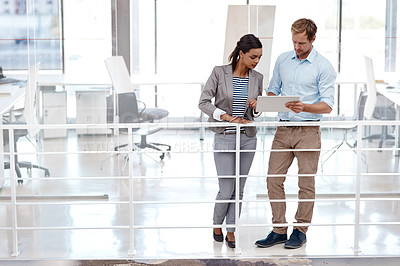 Buy stock photo Full length shot of two good looking colleagues standing at work discussing ideas on a tablet in the office