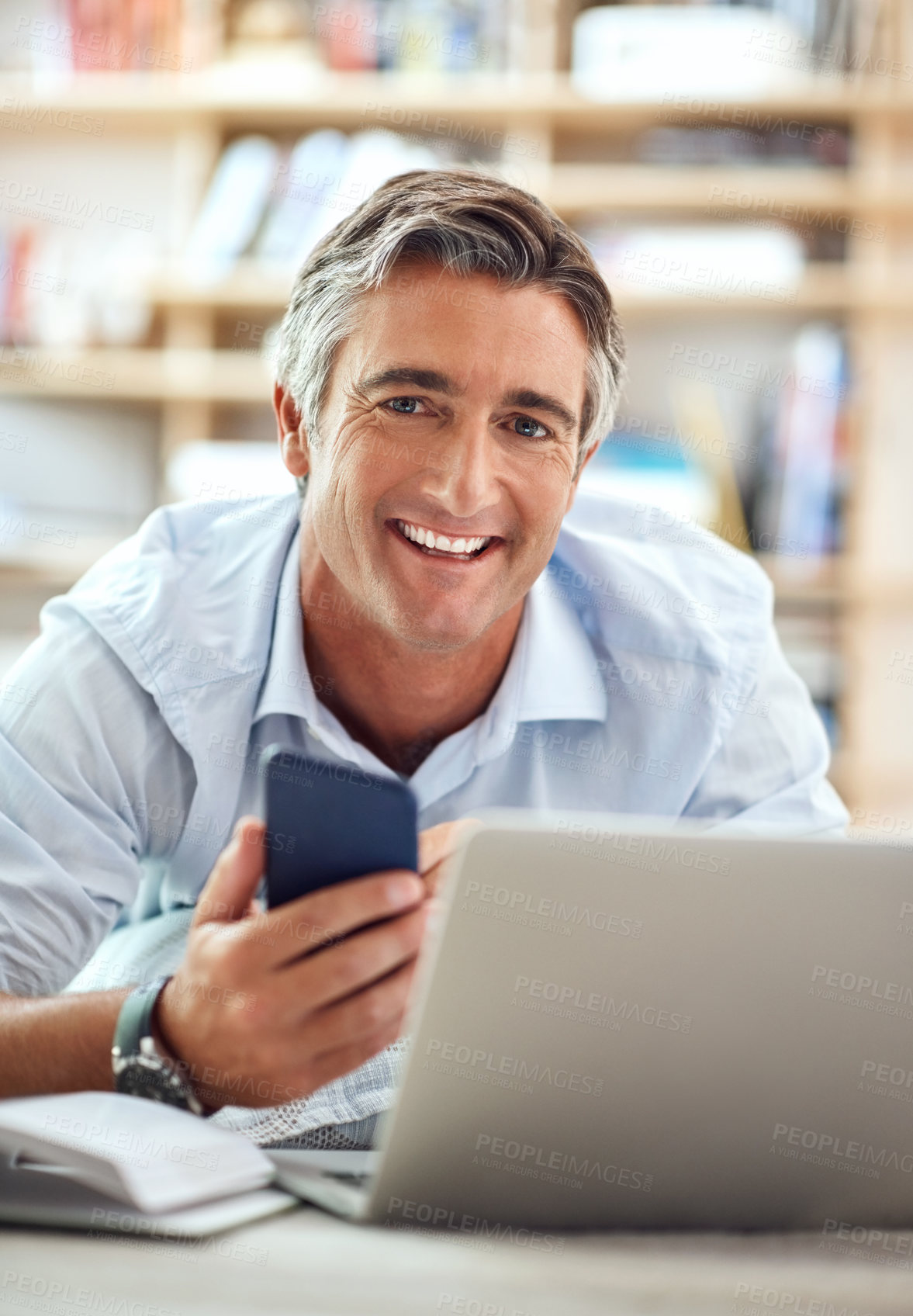 Buy stock photo Cropped portrait of a handsome mature man lying on his living room floor using a cellphone and laptop