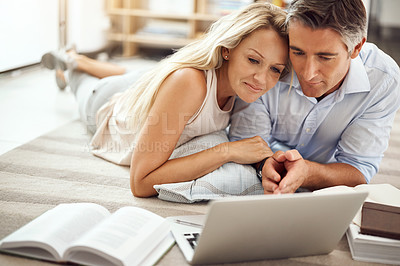 Buy stock photo Cropped shot of an affectionate mature couple lying on their living room floor doing some online research