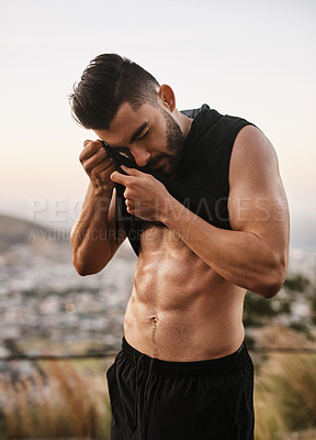 Buy stock photo Shot of a sporty young man wiping the sweat from his forehead with his top while exercising outdoors