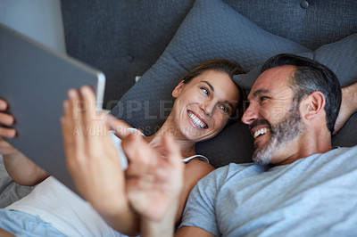 Buy stock photo High angle shot of an affectionate couple using a digital tablet while lying in bed together in the morning