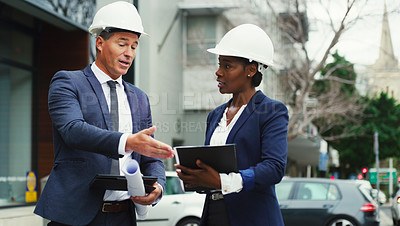 Buy stock photo Shot of two businesspeople wearing hard hats having a discussion outdoors in the city