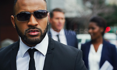 Buy stock photo Shot of a handsome young businessman walking in the city with his colleagues behind him in the background
