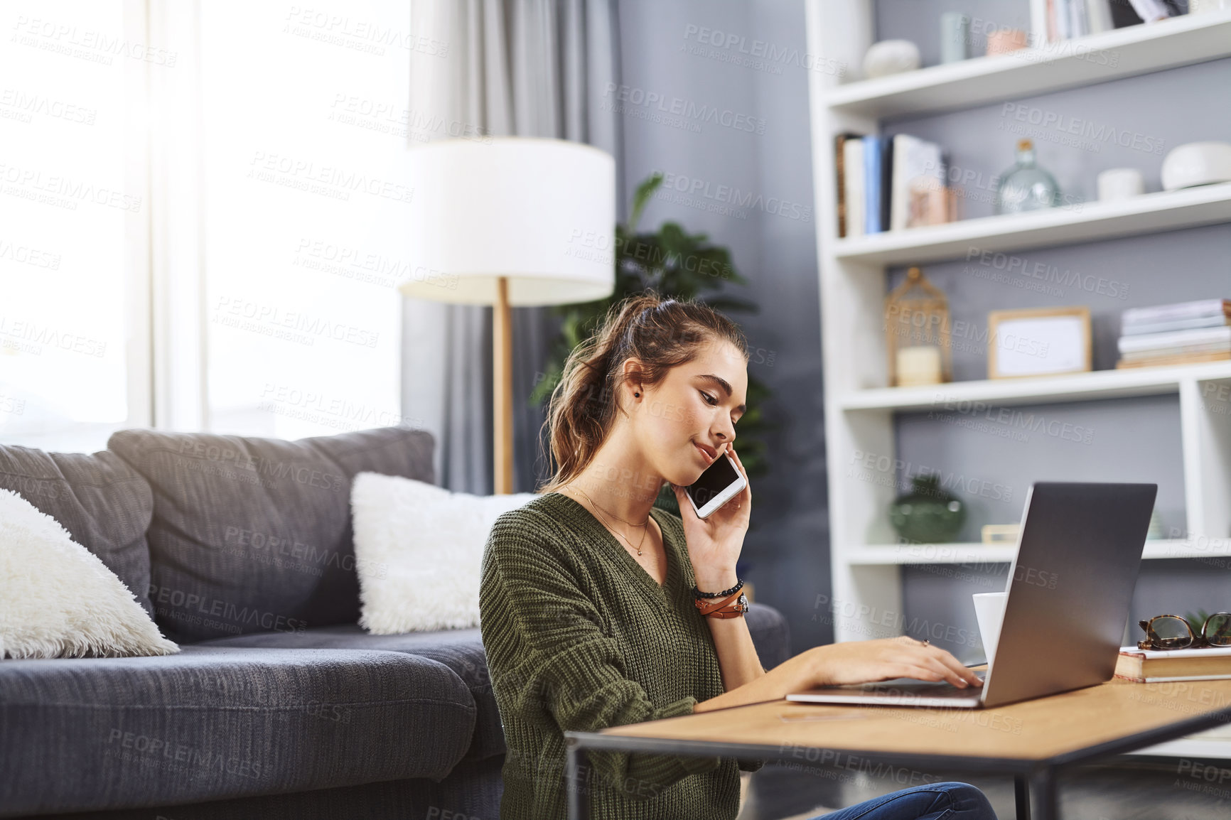 Buy stock photo Shot of a beautiful young woman taking a phone call while working on her laptop at home
