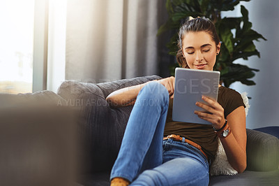 Buy stock photo Shot of a beautiful young woman using her digital tablet while relaxing on a couch at home