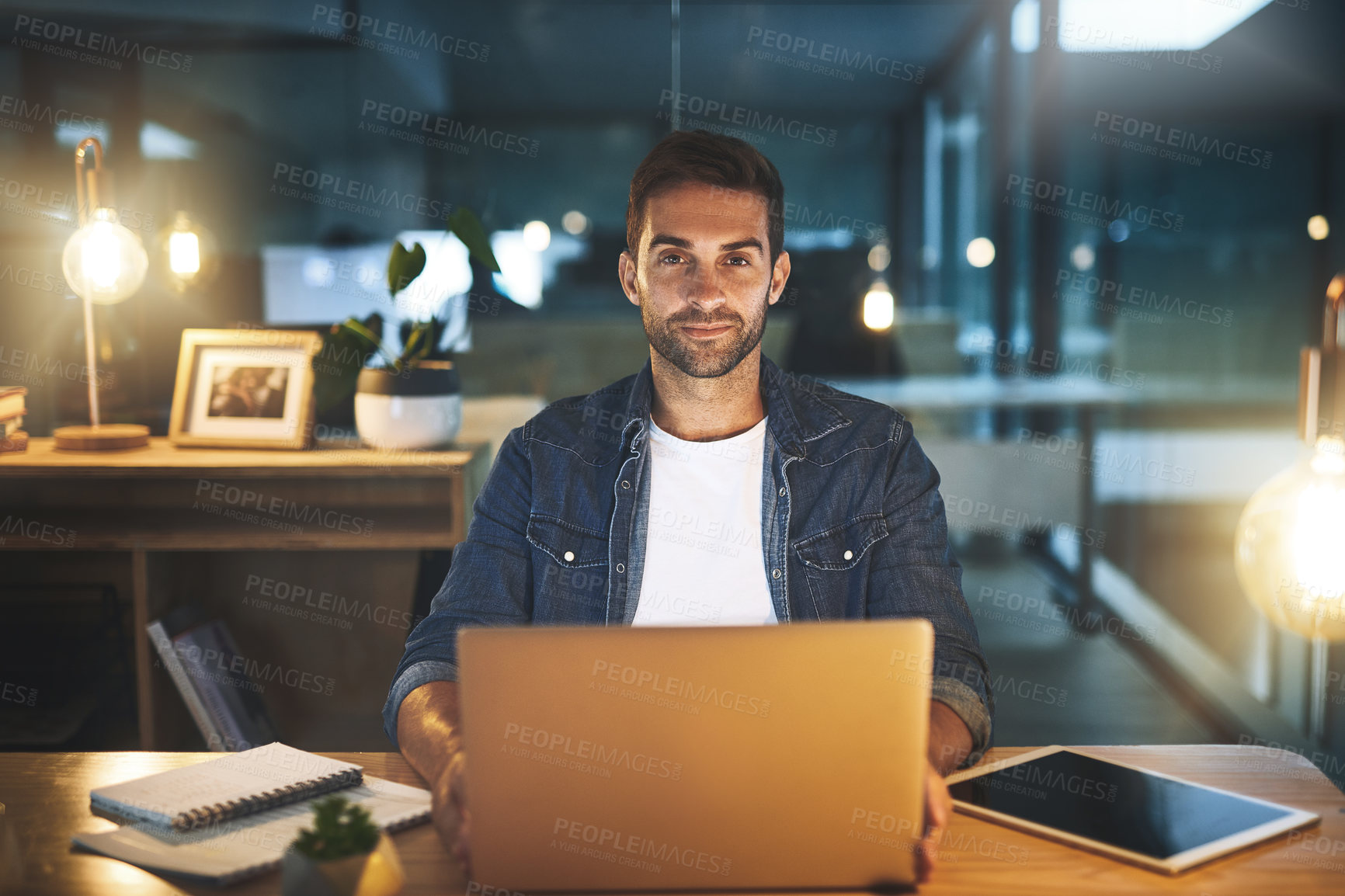Buy stock photo Portrait of a handsome young businessman working late at night on his computer in a modern office