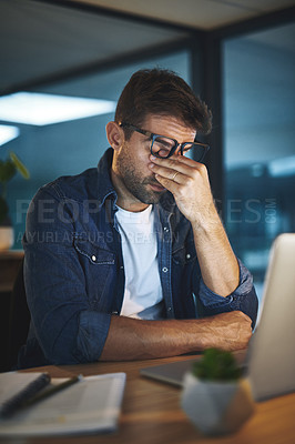 Buy stock photo Shot of a handsome young businessman feeling stressed while working late at night in a modern office