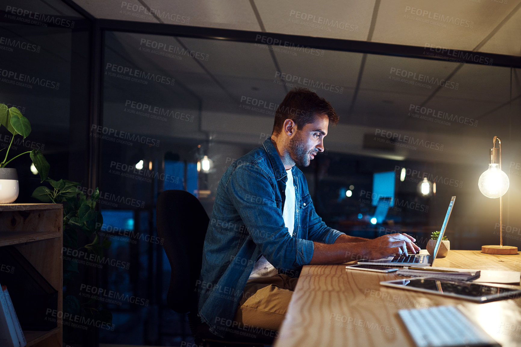 Buy stock photo Shot of a handsome young businessman working late at night on his computer in a modern office