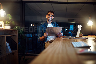 Buy stock photo Portrait of a handsome young businessman smiling while working late at night on his tablet in a modern office