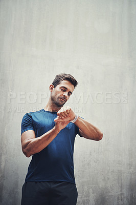 Buy stock photo Shot of a sporty young man checking his watch while exercising outdoors