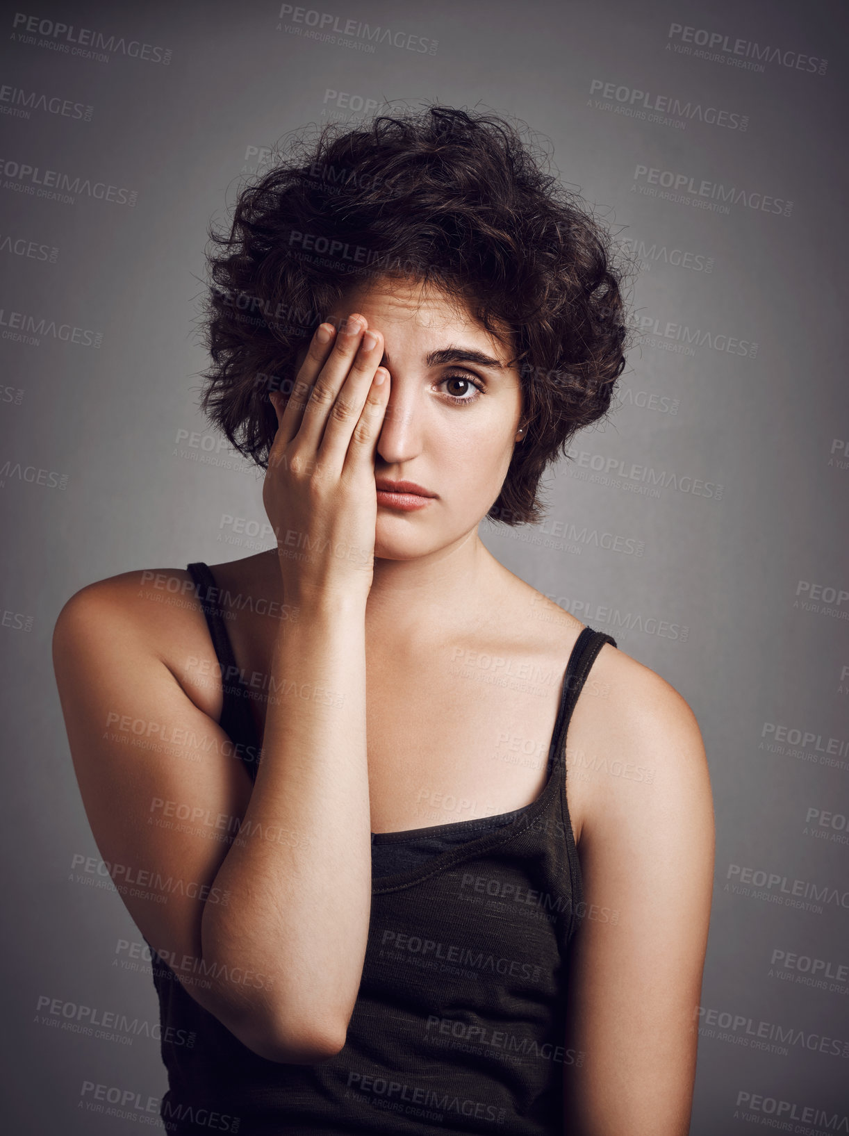 Buy stock photo Studio portrait of an attractive young woman covering her eye with her hand against a grey background