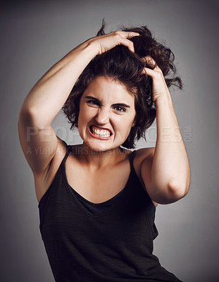 Buy stock photo Studio portrait of an attractive young woman pulling her hair with rage while standing against a grey background