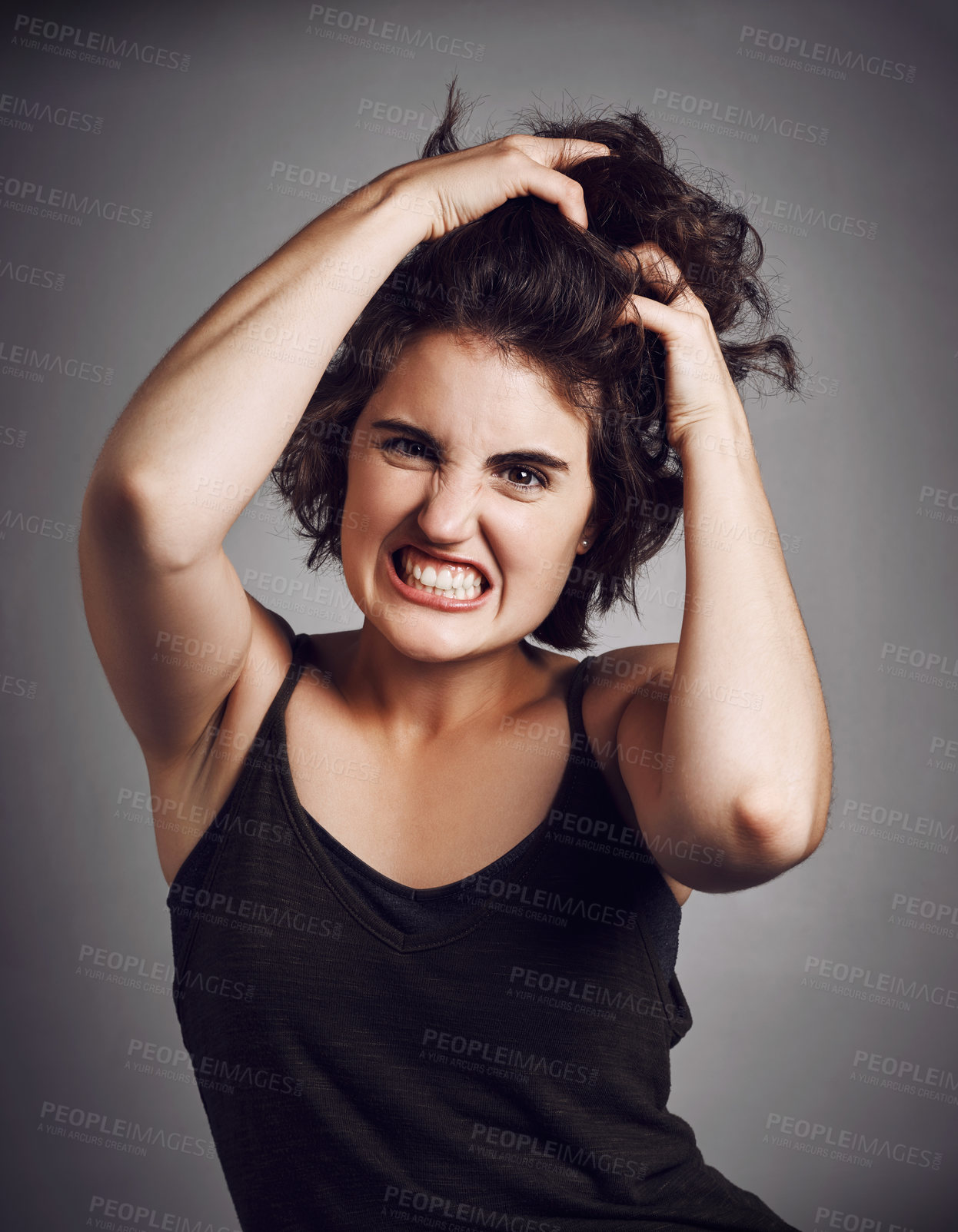 Buy stock photo Studio portrait of an attractive young woman pulling her hair with rage while standing against a grey background