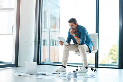 Buy stock photo Shot of a young businessman brainstorming with a digital tablet and paperwork on a floor in an office