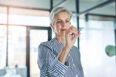 Buy stock photo Shot of a mature businesswoman writing down notes on a glass wall in her office