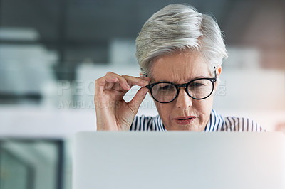 Buy stock photo Shot of an attractive mature businesswoman adjusting her glasses while working on  a laptop in her office