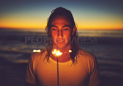 Buy stock photo Shot of a young man holding a sparkler at the beach at night