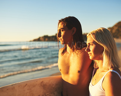 Buy stock photo Cropped shot of a young couple with a surfboard standing together and watching the sunset on the beach